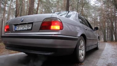 Chernigov, Ukrayna - 6 Ocak 2021: Eski BMW 7 Serisi (E38) ormanda yolda. Kasvetli hava. Farları açık araba.
