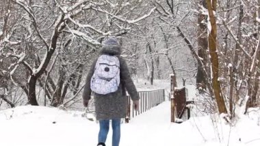 Sırt çantalı bir kız eski köprü boyunca kış ormanında yürüyor.