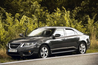 Chernigov, Ukrayna - 24 Temmuz 2021: Saab arabası yolda. Ağaçların arka planında Gri Saab 9-5 2010 arabası