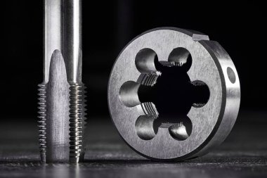 tap, ölüm metal iplikleri kesmek için gerekli bir araçtır. Ev atölyesinde küçük bir iş için çilingir aksesuarları. Karanlık arka plan. Makro