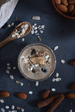 Tasty smoothie with banana and oatmeal, muesli and almond milk in a glass. On a dark gray concrete stone background, with ingredients for cooking. Bio. Top view.