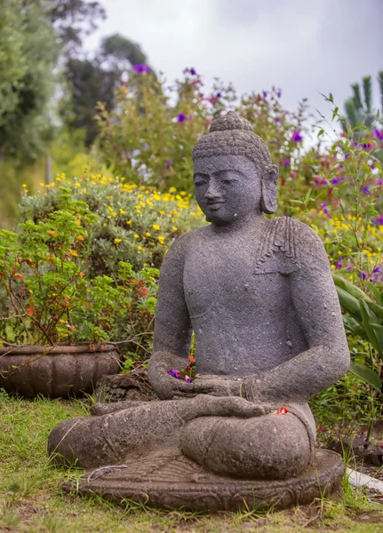 Estatua de Buda de piedra rodeada de flores — Foto de Stock