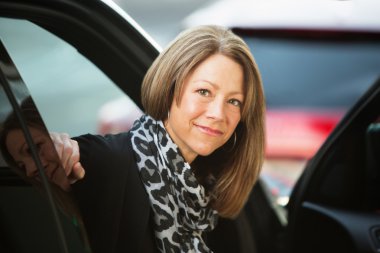 Businesswoman looking at camera and sitting in car clipart