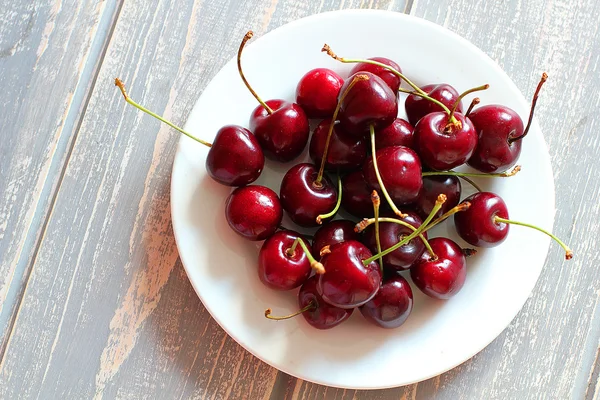 Cerejas em placa branca na mesa cinza de madeira . — Fotografia de Stock