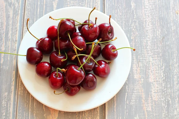 Cerejas em placa branca na mesa cinza de madeira . — Fotografia de Stock