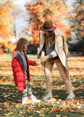 Anne ve kızı sonbahar parkında sarılıp öpüşüyorlar.