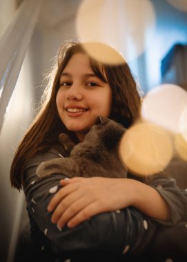 Gri pijamalı kızlar merdivenlerde oturan mavi kediyi kucaklıyor.