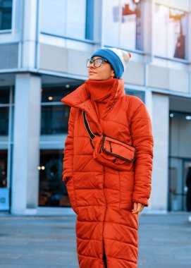 Kırmızı ceketli, şapkalı, soğuk havada şehirde yürüyen mutlu bir kadın.