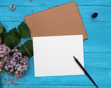 Bir el işi zarf, beyaz kağıt, leylak brunch, ısıtma, klasik turkuaz ahşap arka planda mum.