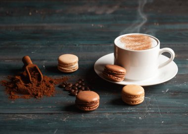 Bir fincan kahve, kahve çekirdeği, öğütülmüş kahve ve ahşap arka planda badem kurabiyesi.