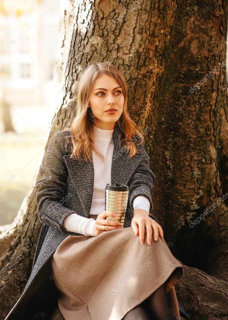 woman in grey coat drinking coffee in the park
