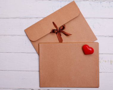 Beyaz ahşap arka planda iki el işi zarf ve kırmızı kalp