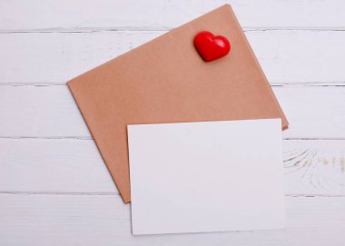 Beyaz ahşap arka planda beyaz kağıt ve kırmızı kalp.