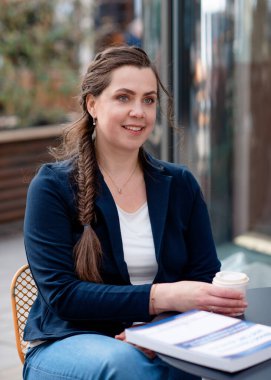 Bir kadın kafede oturuyor, kahve içiyor ve ders çalışıyor.