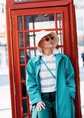 Güneş gözlüklü kadın, sıcak ve turkuaz hendek İngiliz şehrinde yürüyor.