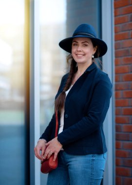 Şapkalı ve kot pantolonlu bir kadın bahar günü sokakta yürüyor.