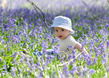 Kot pantolonlu ve mavi şapkalı küçük çocuk çan çiçekleri arasında parkta oynuyor.