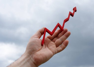 Eller bulutlu gökyüzüne karşı kırmızı bir grafik tutuyor