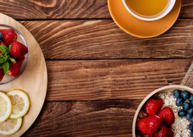 Çilek, yaban mersini ve yulaf ezmesi kaselerde ve ahşap arka planda sarı çay.