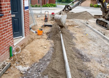 Yaya yolu inşaatı sırasında kenar kaldırım döşeme yeni konut geliştirme üzerine yeni inşa evinin önünde ve çevresine kazıcı ile yarı-beton yerleştirme.