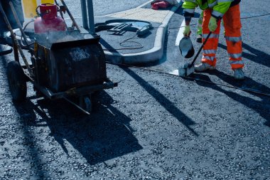 Yeni kavşak ve yol inşaatı sırasında yeni döşenmiş asfalt üzerinde termoplastik yol işareti uygulayan yol işçisi