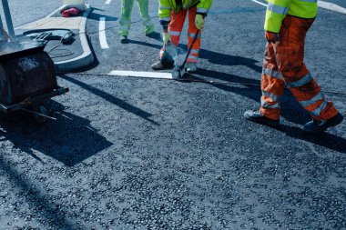 Yeni kavşak ve yol inşaatı sırasında yeni döşenmiş asfalt üzerinde termoplastik yol işareti uygulayan yol işçisi
