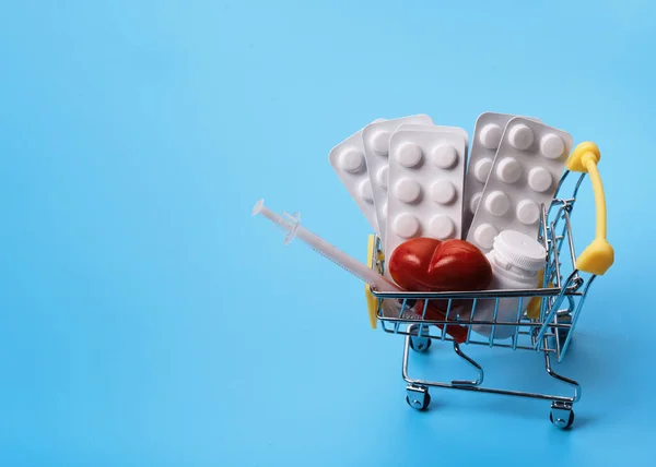 pills, vitamins and disposable syringe in shop trolley on blue background