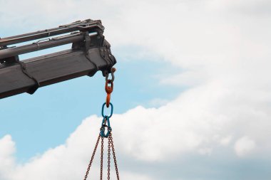 Beyaz bulutlu açık mavi gökyüzüne asılı vinç kancası ve zincirlerinin yakın çekimi..