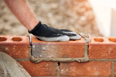 Eldivenli inşaat işçilerinin yakın çekimleri duvara havan topu ile tuğla koyuyor..