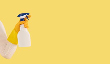 A person wearing yellow gloves holds a white spray bottle against a yellow background.