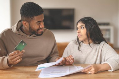 Genç bir çift, ellerinde kredi kartı ve faturalar tutarken bir masada oturup mali durumlarını tartışıyor..