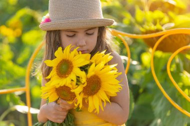 Hasır şapkalı genç bir kız önünde bir buket ayçiçeği tutuyor..
