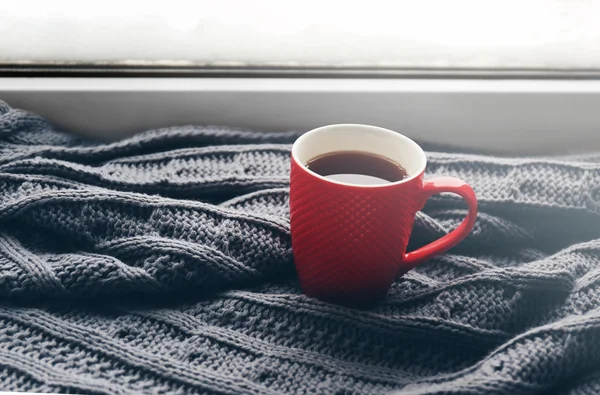 Tasse de thé rouge et tresse tricotée chaude sur le rebord de la fenêtre, gros plan — Photo