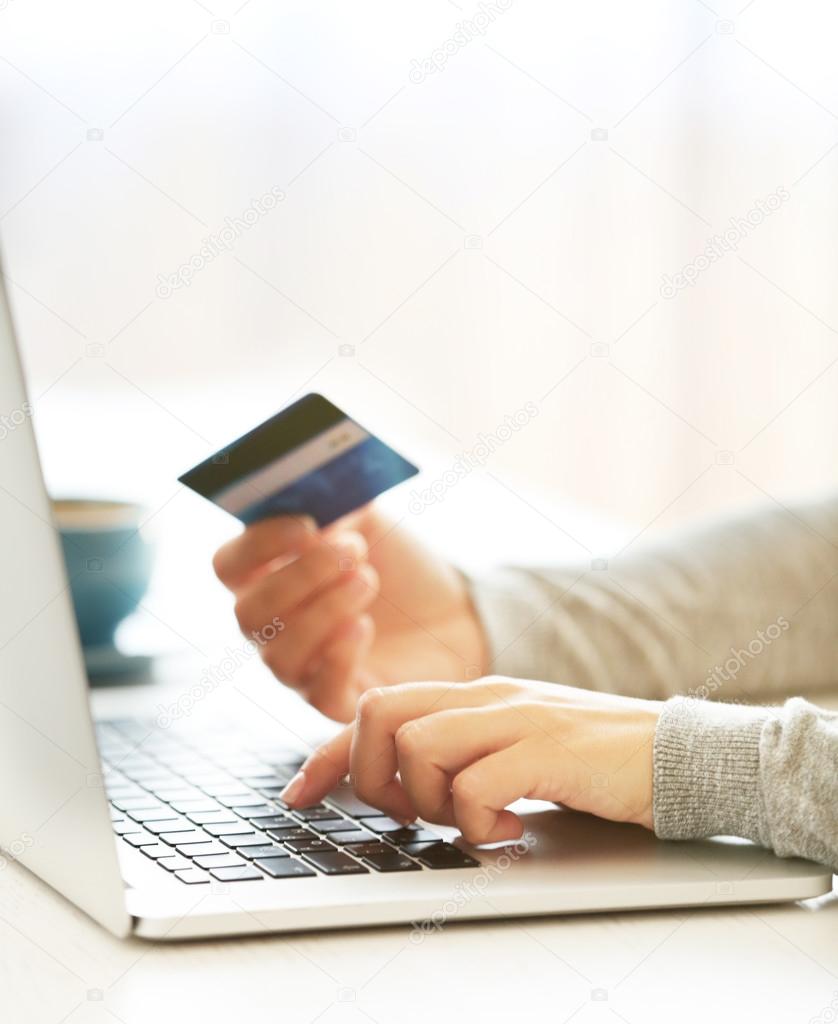 E-commerce concept. Woman with credit card, laptop and cup of coffee, close up