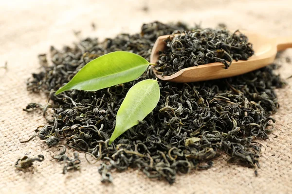 Scattered tea with green leaves in wooden spoon on burlap background — Stock Photo, Image