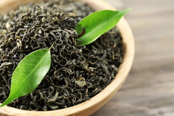 Dry tea with green leaves in bowl on wooden table background — Stock Photo, Image