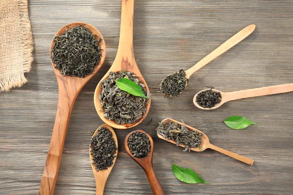 Té seco con hojas verdes en cucharas de madera sobre fondo de mesa —  Fotos de Stock