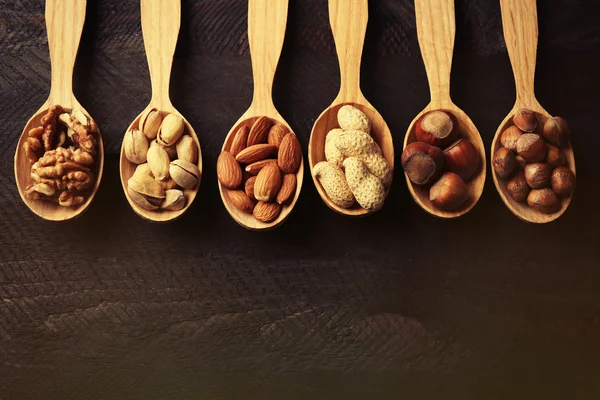 Lepels met hazelnoten, walnoten, pistachenoten, amandelen, eikels en pinda's, op grijze houten achtergrond — Stockfoto