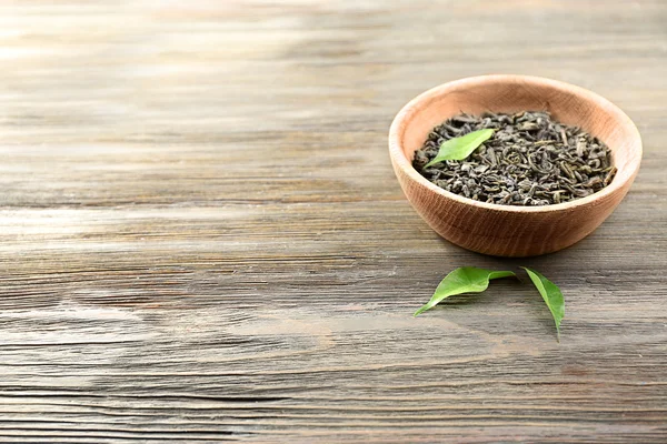 Сухой чай с зелеными листьями в миске на деревянном фоне стола, пространство для копирования — стоковое фото