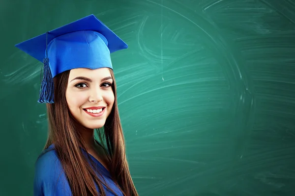 グリーン黒板背景に卒業の帽子を持つ若い女性 — ストック写真