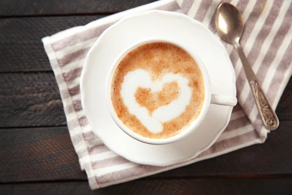 Filiżankę gorącej cappuccino z krem serca i łyżka na czarny drewniany stół — Zdjęcie stockowe