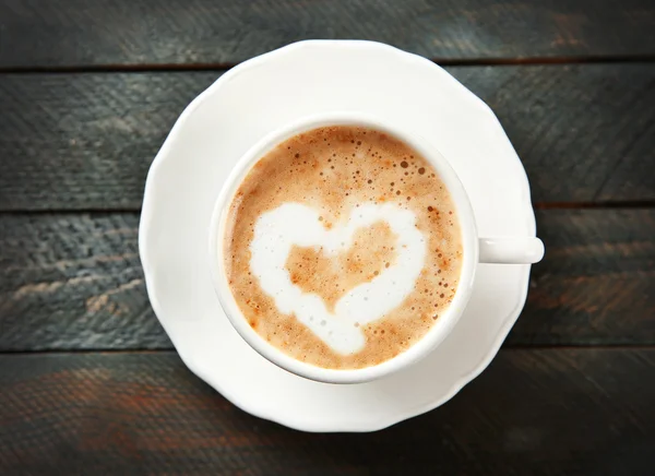 Cup of hot cappuccino with cream heart on a black wooden table