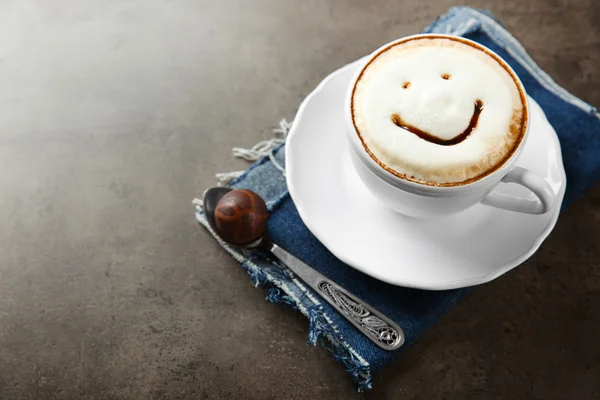 Tasse mit heißem Cappuccino mit Schokoladensirup und Bonbons auf grauem Tisch — Stockfoto