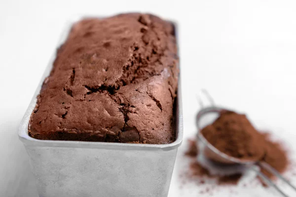 Kue coklat dalam baking dish dengan bubuk kakao di atas meja putih — Stok Foto