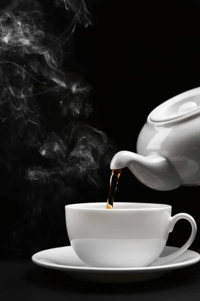黒の背景の上にカップに釜から熱いお茶を注いで、クローズ アップ — ストック写真