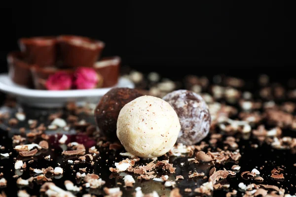 Doces de chocolate sortidas com flocos no fundo preto — Fotografia de Stock