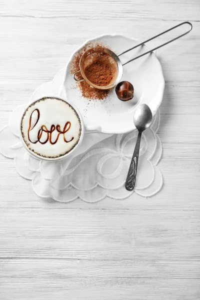 Cup of cappuccino with chocolate syrup and cacao powder on light wooden table — Stock Photo, Image