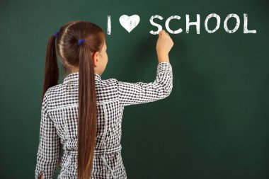 Güzel küçük bir kız sınıfta yazı tahtası üzerinde yazıyor