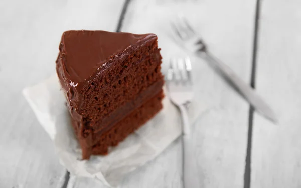 Un pedazo de pastel de chocolate con tenedores sobre fondo de mesa de madera, primer plano —  Fotos de Stock