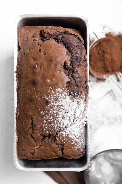 Шоколадный торт в выпечке блюдо с какао порошок на белый стол — стоковое фото